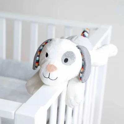 Peluche sonore à bruit blanc Dex le chien signée Zazu, sur le rebord du lit Peluche sonore à bruit blanc Dex le chien signée Zazu, sur le rebord du lit